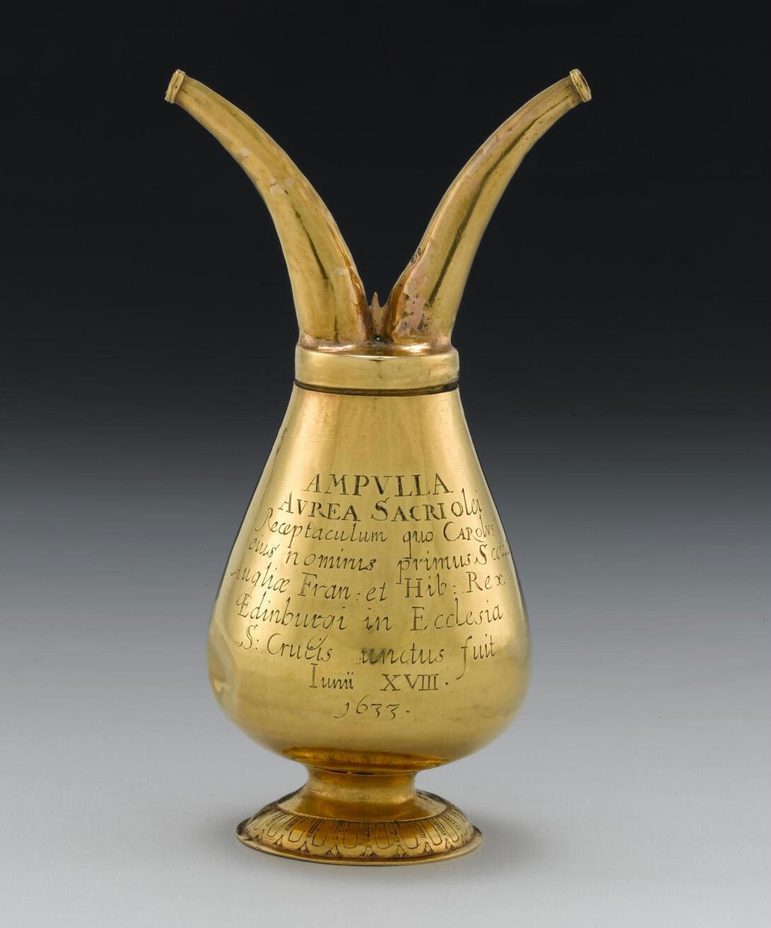 A short-stemmed gold vessel, wide at the bottom and narrow top with two hoses attached to the top and engraved text to the body of the vessel.
