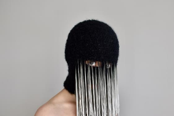 A woman wearing a black balaclava mask with long silvery threads hanging from beneath her eyes.
