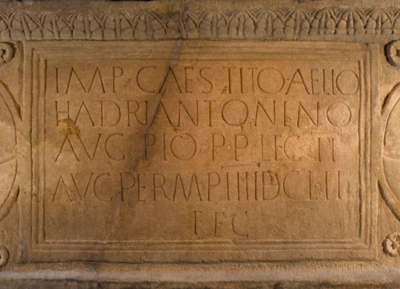 Close-up of an orange stone slab with Latin text written in neat rows across its whole surface.