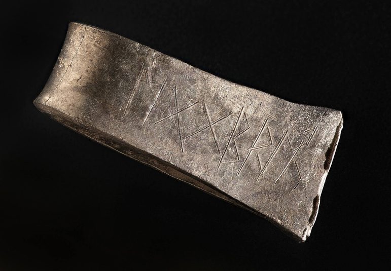 A piece of tarnished silver wrapped in a loop with runes etched on its surface