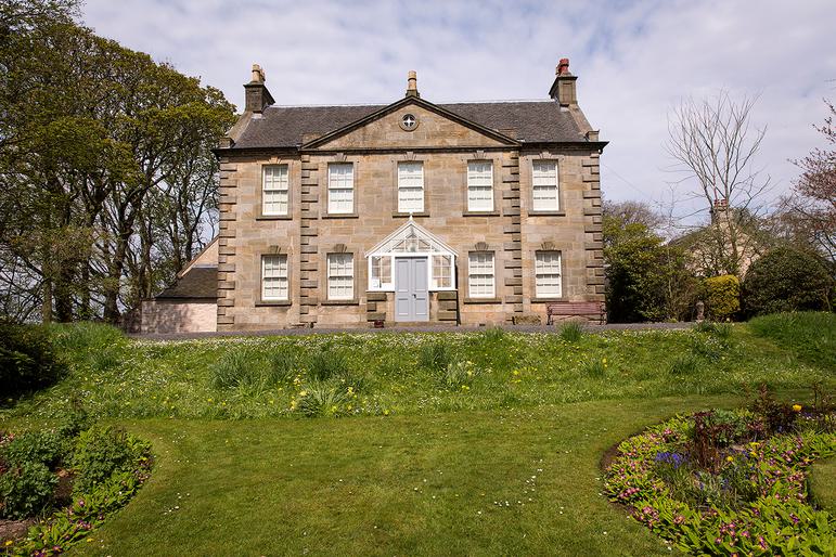 A photo of a detached house at the top of a raised grassed garden.
