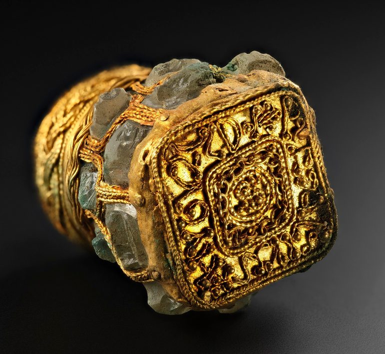 Gold-wrapped jar laid on its side with the base facing forward. Gold thread forms letters around its edge.