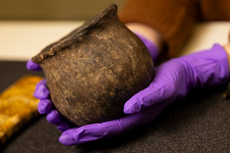 A small brown earthenware ceramic vessel with a wide neck and round body. The neck is slightly misshapen.