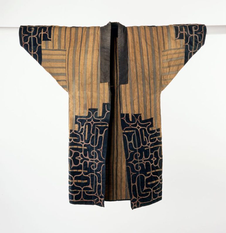 A light brown and navy long jacket with wide sleeves laid flat. The cuffs and bottom of the jacket are decorated in navy with an abstract pattern.
