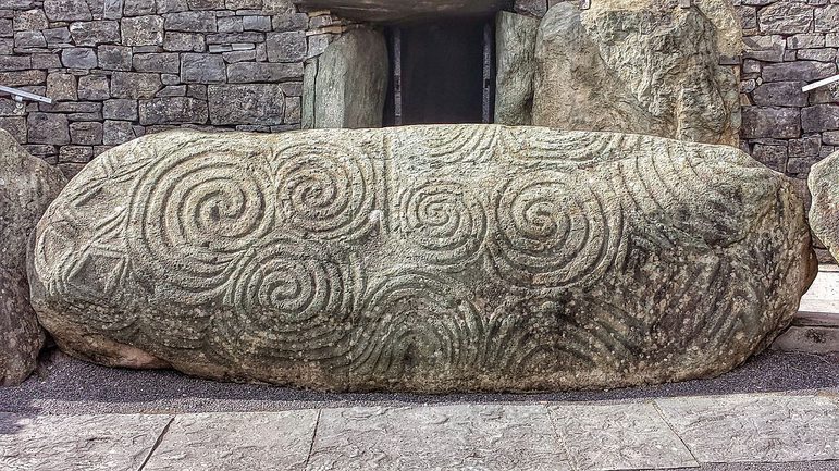 A yellow oval square rock, carved with large spiral and diamond shaped decorations.