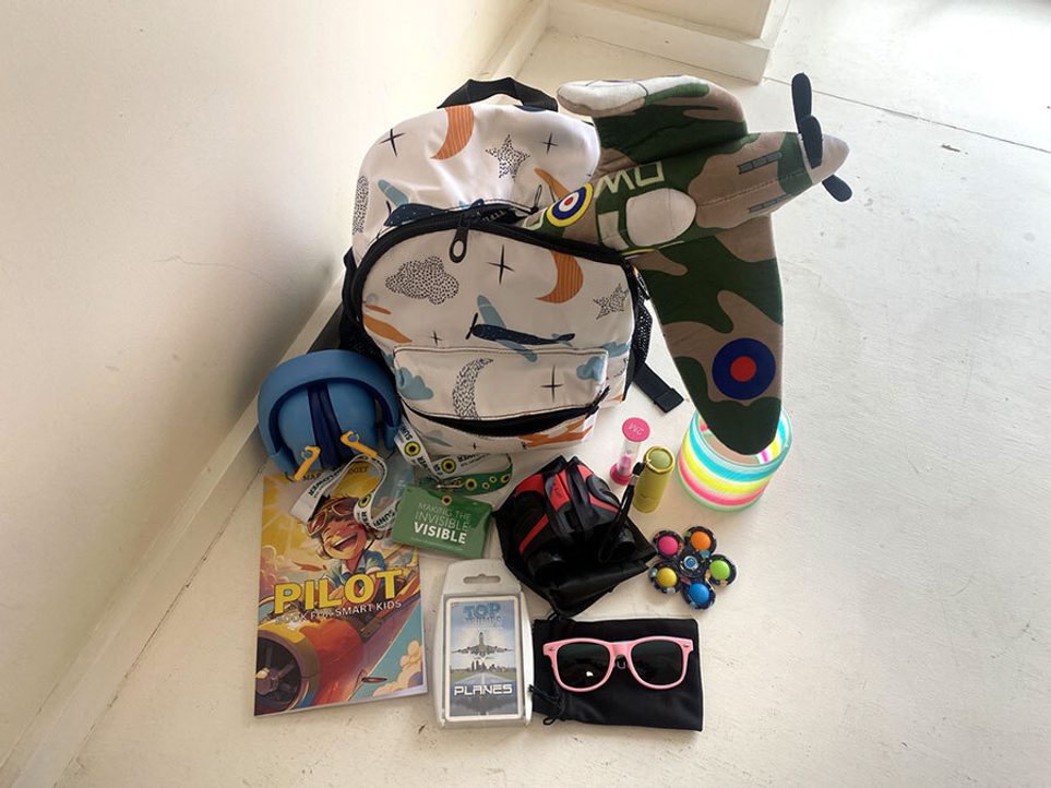An open patterned white backpack surrounded by a variety of sensory toys and objects.