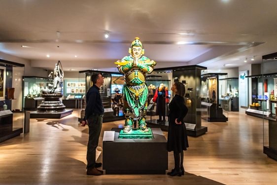 Two visitors in a museum gallery looking up at a sculpture of Weituo.
